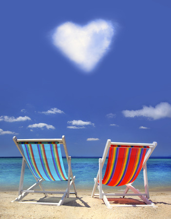 Två solstolar på stranden med hjärtformat moln på himle
